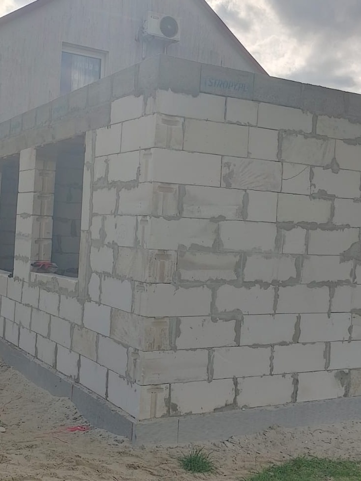 Budowa ściany zewnętrznej z białych bloczków, widoczny fragment budynku z oknem i klimatyzatorem, etap murowania.