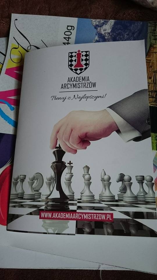 Broszura reklamowa Akademii Arcymistrzów z grafiką dłoni przesuwającej czarnego króla na szachownicy.
