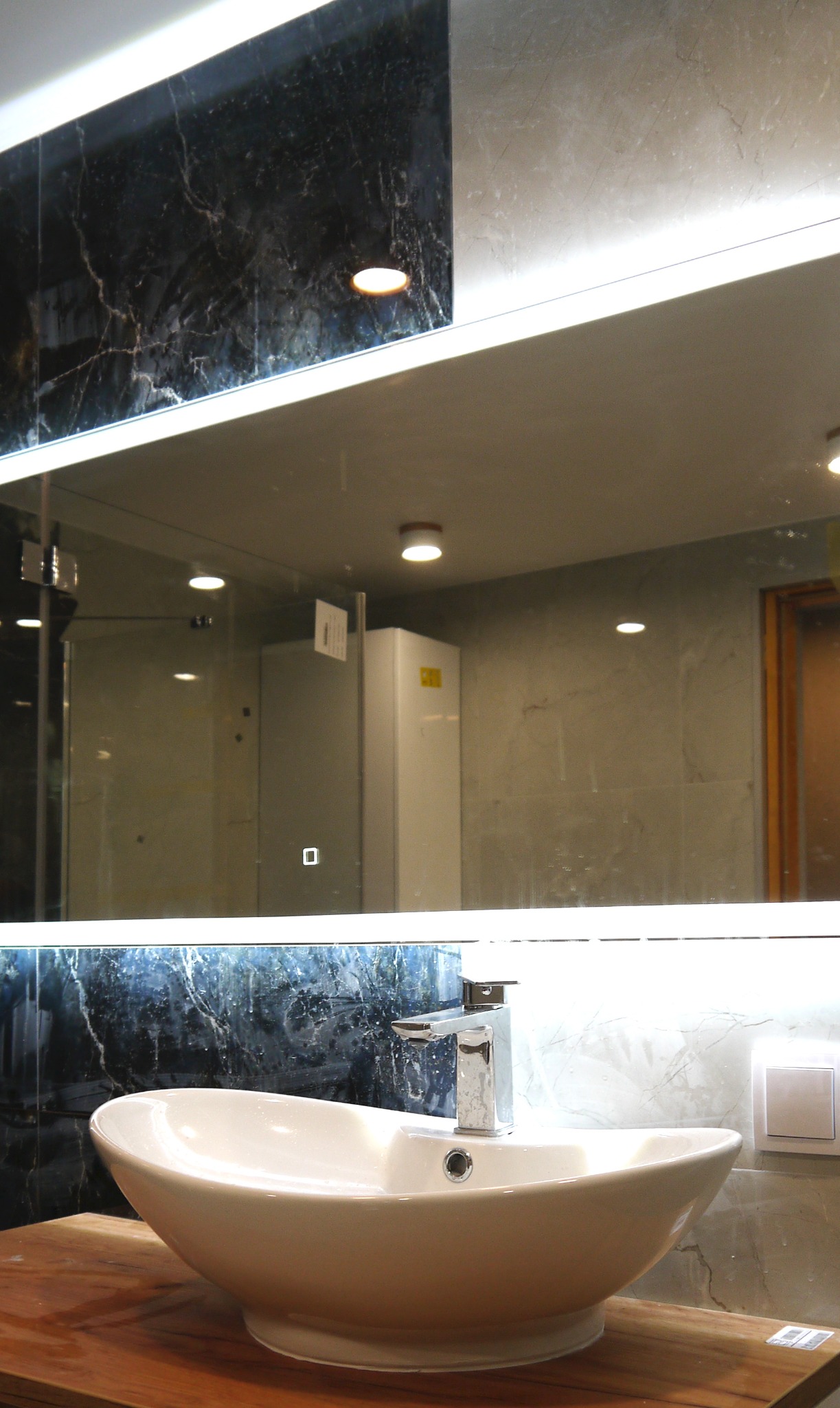 Owalna umywalka nablatowa z chromowaną baterią, zamontowana na drewnianym blacie, z podświetlanym lustrem i czarnym marmurem w tle