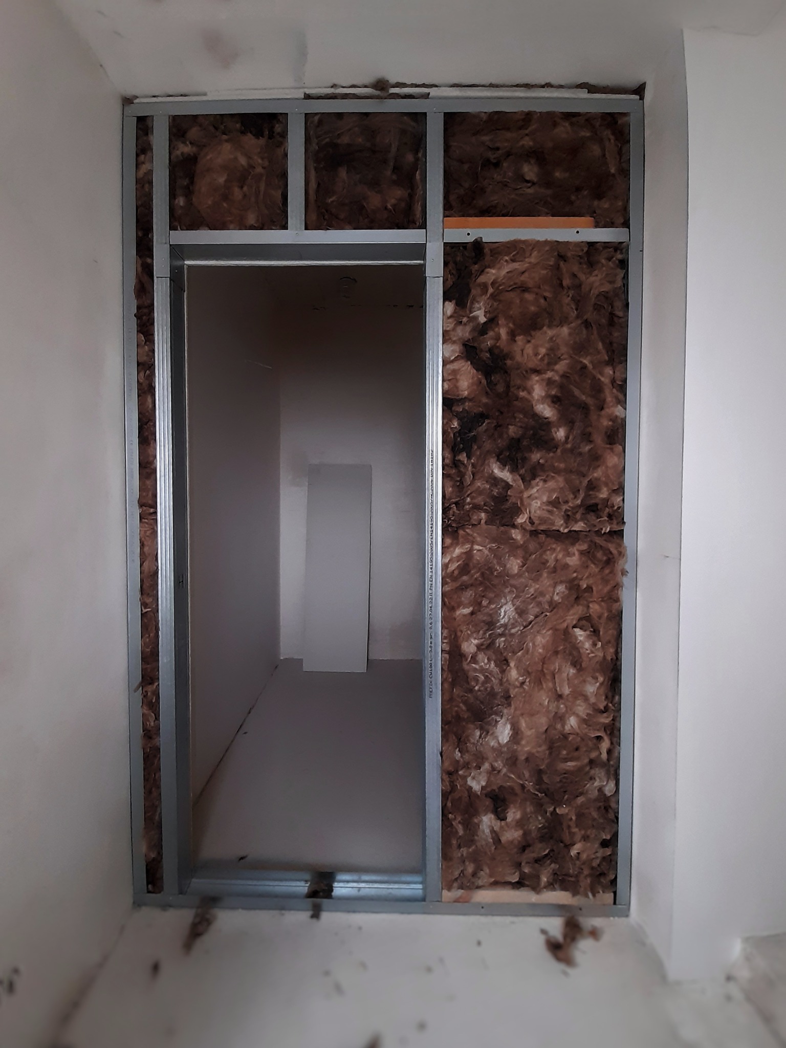 Wnętrze ściany z widoczną izolacją z wełny mineralnej i metalową konstrukcją nośną, przygotowane do dalszych prac wykończeniowych.