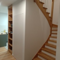 GRZEGORZ OKRAJEK SPEC-REM - Jasne drewniane schody z białymi podstopnicami, zabudowa regałowa z jasnego drewna i białe ściany w nowoczesnym wnętrzu.