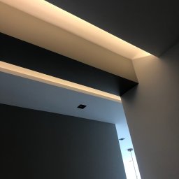 GRZEGORZ OKRAJEK SPEC-REM - Nowoczesne wykończenie sufitu z oświetleniem LED w Dąbrowie Górniczej, widok pod kątem, ciemnoszare ściany i białe elementy dekoracyjne.