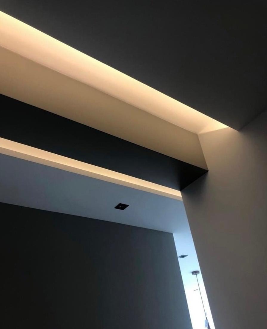 Nowoczesne wnętrze z podwieszanym sufitem i oświetleniem LED w ciepłej barwie, widok z dołu na kontrastowe połączenie czerni i bieli na ścianach.