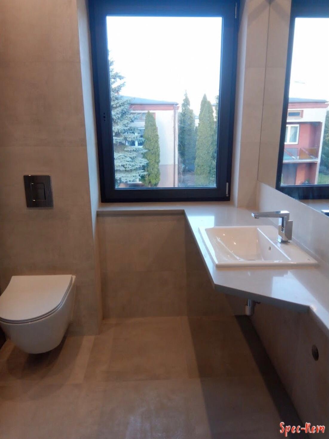 Nowoczesna łazienka z podwieszaną toaletą, umywalką nablatową i dużym oknem z widokiem na zieleń, wykończona w beżowych odcieniach płytek.