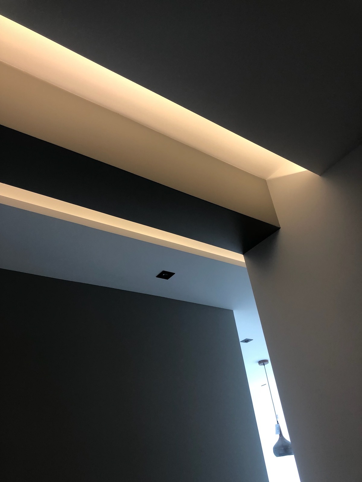 Nowoczesne wykończenie sufitu z oświetleniem LED w Dąbrowie Górniczej, widok pod kątem, ciemnoszare ściany i białe elementy dekoracyjne.