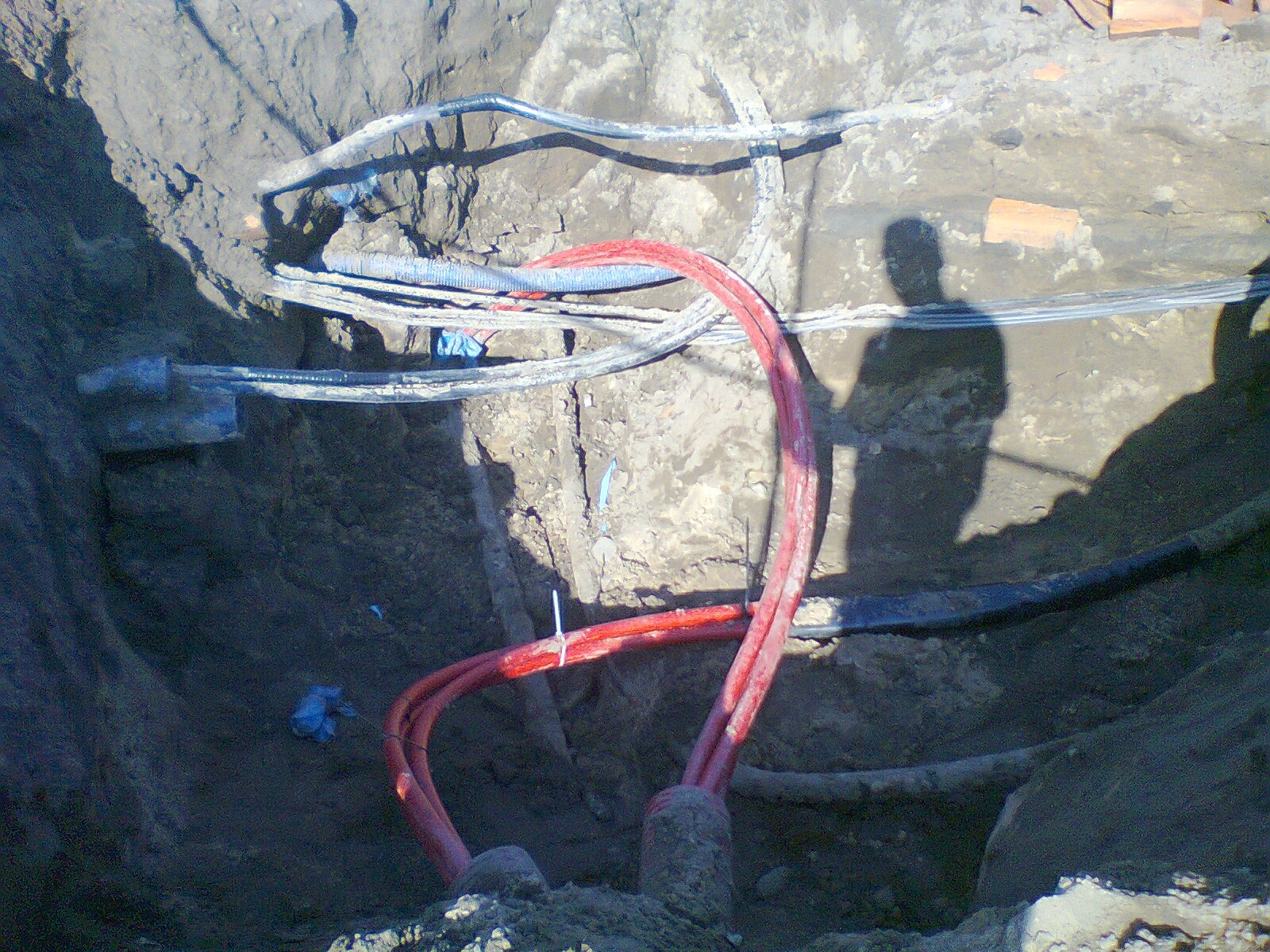 Wykop z ułożonymi kablami w ziemi, widoczny cień osoby nadzorującej prace.