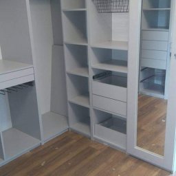 NA WYMIAR Agnieszka Janeczko - Jasnoszara szafa wnękowa z koszami i lustrzanymi drzwiami przesuwnymi, widok z dołu, drewniana podłoga, skośny sufit.