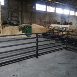 JSMP SYSTEM SPÓŁKA Z OGRANICZONĄ ODPOWIEDZIALNOŚCIĄ - Surowa, spawana metalowa balustrada w warsztacie, z widocznymi śladami obróbki i stertą wiórów drzewnych w tle, oświetlona przez okna dachowe.