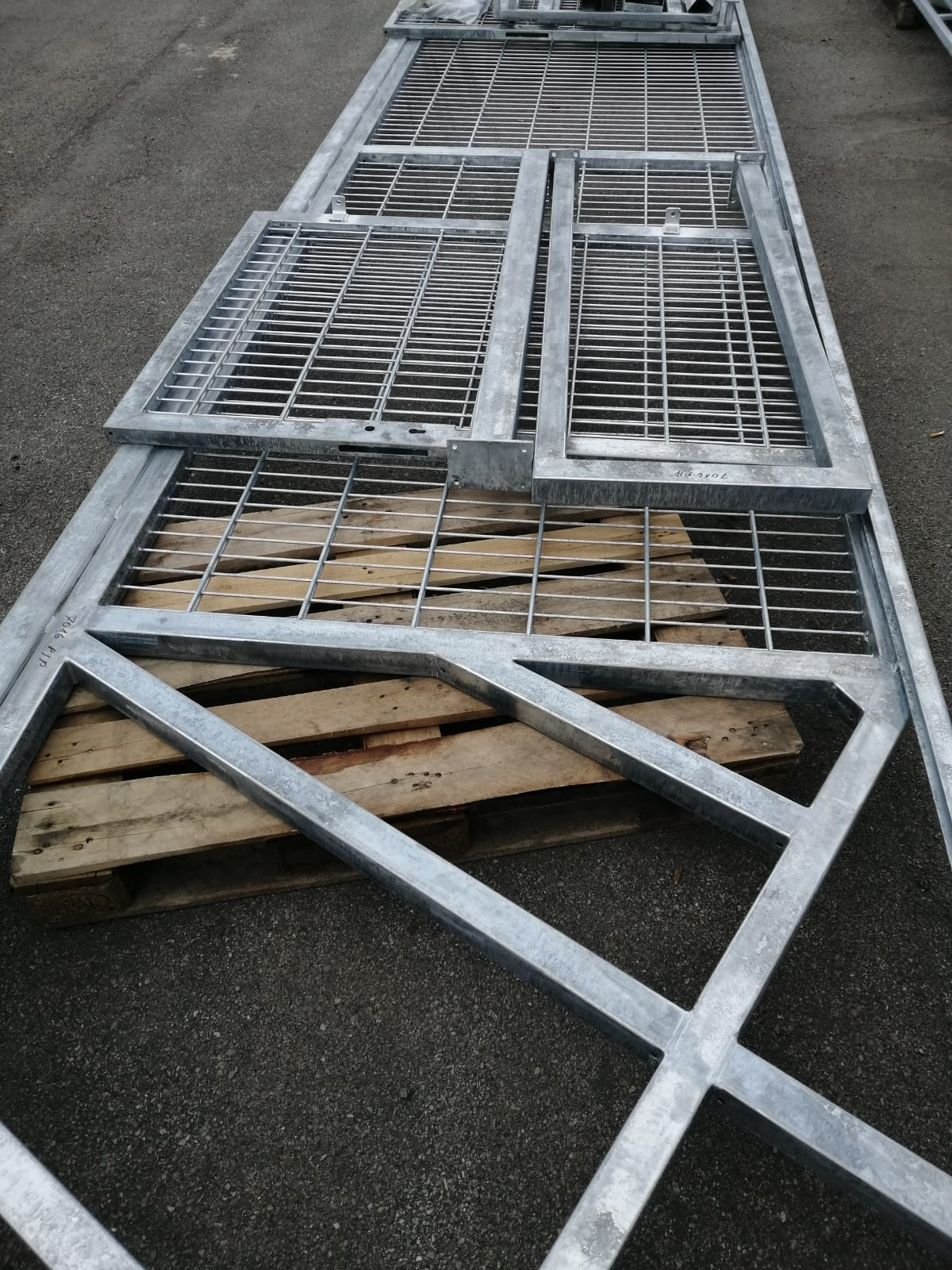Elementy metalowej bramy wjazdowej z kratownicą, leżące na drewnianej palecie na tle asfaltu.