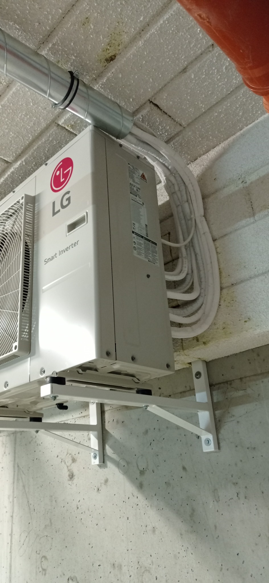 Biała jednostka wewnętrzna klimatyzacji LG Smart Inverter zamontowana na metalowym wsporniku, z widocznymi przewodami w białej izolacji, prowadzonymi wzdłuż sufitu z betonu komórkowego.