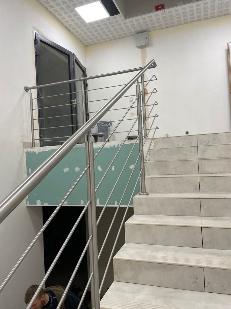 Nowoczesna balustrada ze stali nierdzewnej na schodach z płytek, widok z dołu, z elementami wykończeniowymi ścian w tle. Minimalistyczny design.