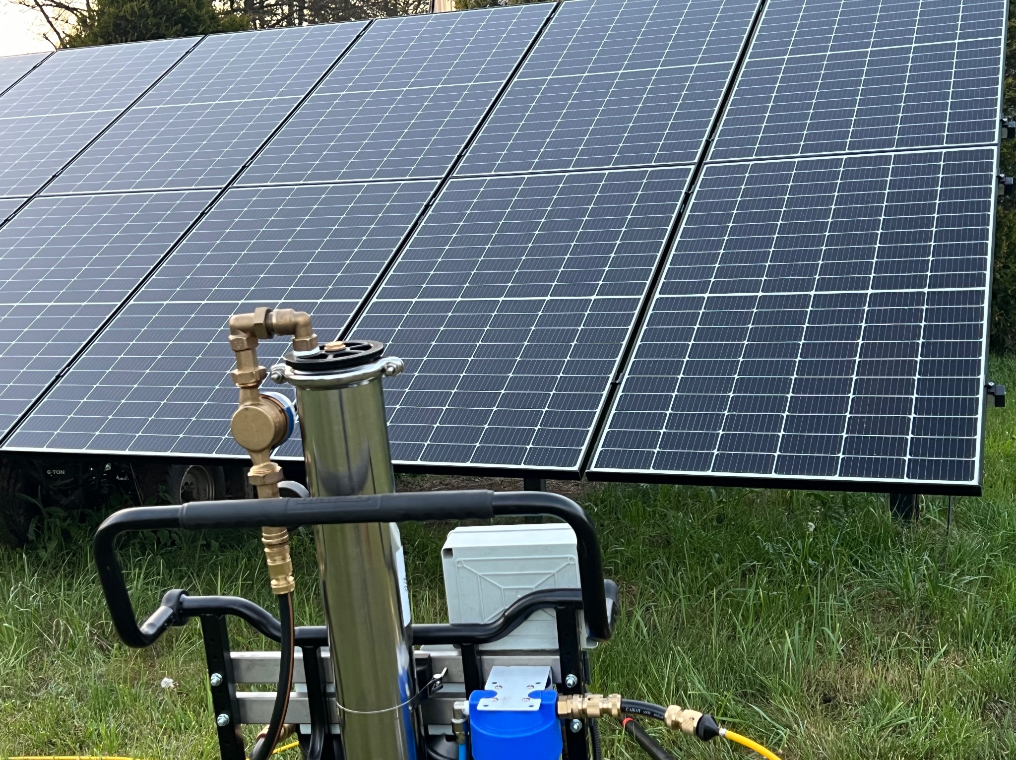 Mobilny system myjący z lancą teleskopową przed panelami słonecznymi na zielonej trawie. Urządzenie do czyszczenia paneli fotowoltaicznych.