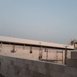 Emilian Wojtczak - Budowa hali przemysłowej z bloczków betonu komórkowego Ytong, widoczne zbrojenia i konstrukcja dachu w trakcie montażu, księżyc na niebie.