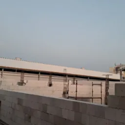 Budowa hali przemysłowej z bloczków betonu komórkowego Ytong, widoczne zbrojenia i konstrukcja dachu w trakcie montażu, księżyc na niebie.