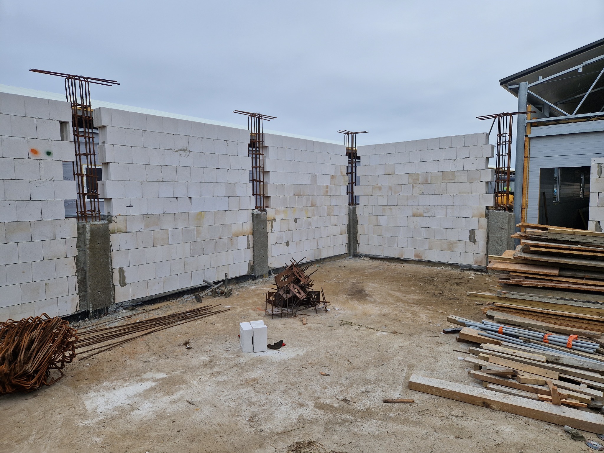 Wznoszenie ścian z betonu komórkowego z widocznym zbrojeniem pionowym, składowane materiały budowlane na placu budowy.