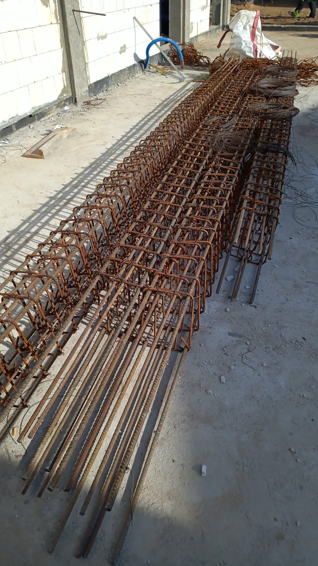 Zestaw zbrojenia fundamentowego ułożony rzędami na placu budowy, widoczne ściany z betonu komórkowego w tle.