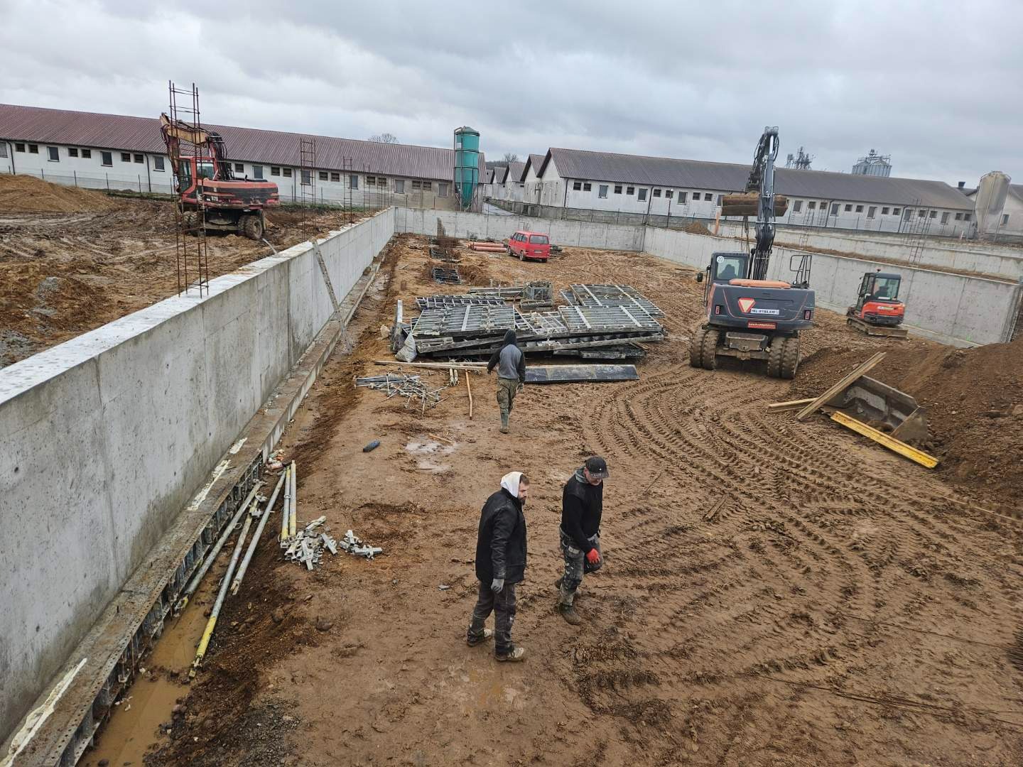 Wykop fundamentowy z betonowymi ścianami, przygotowany do dalszych prac budowlanych, z widocznymi maszynami budowlanymi i elementami szalunków.
