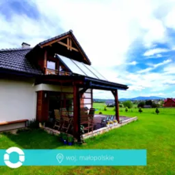 Dom jednorodzinny z zainstalowanymi panelami słonecznymi na dachu, widok z ogrodu, w tle krajobraz Małopolski.