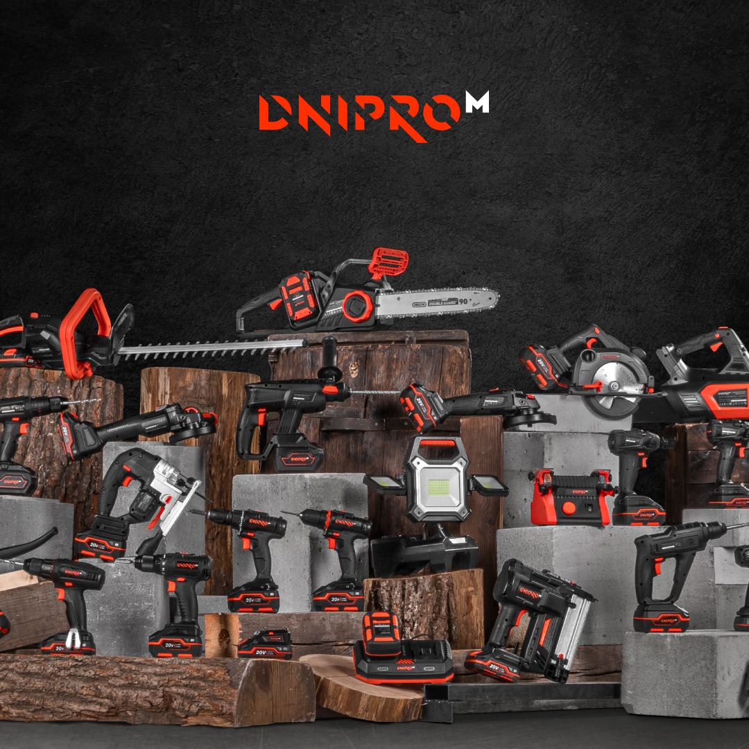 Zestaw elektronarzędzi akumulatorowych w kolorach czarnym i pomarańczowym, w tym wiertarki, piły łańcuchowe, szlifierki i lampa, ułożonych na drewnianych blokach i betonowych kostkach na tle...