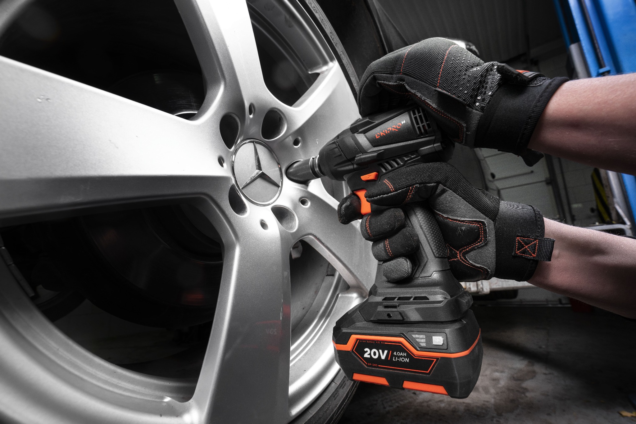 Mechanik w rękawicach roboczych odkręca śrubę w srebrnej feldze samochodu za pomocą akumulatorowego klucza udarowego.