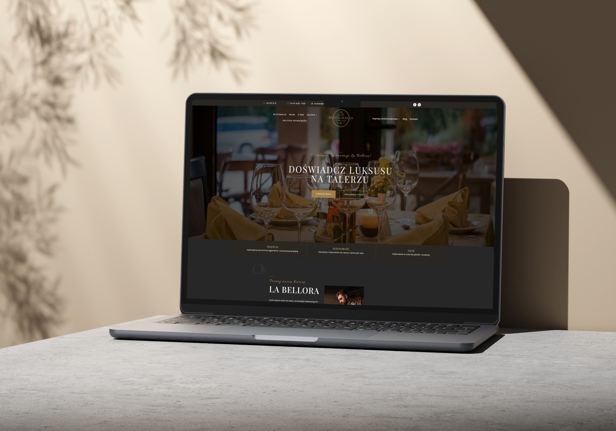 Laptop wyświetla stronę internetową restauracji La Bellora z eleganckim wystrojem i menu. Cienie liści na ścianie dodają naturalnego akcentu do kompozycji.