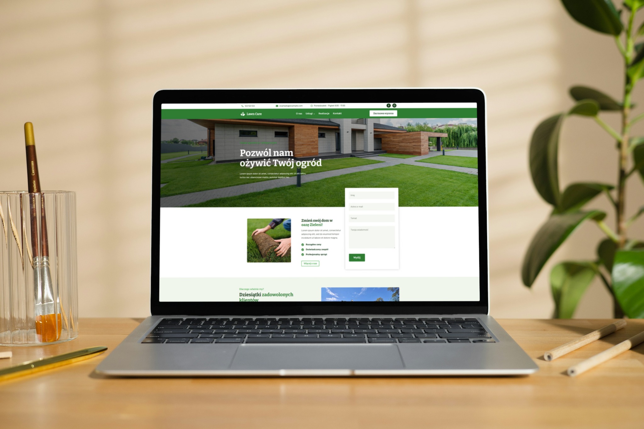 Laptop wyświetla stronę internetową firmy Lawn Care z formularzem kontaktowym i hasłem 'Pozwól nam ożywić Twój ogród'. Na biurku pędzle i ołówek.