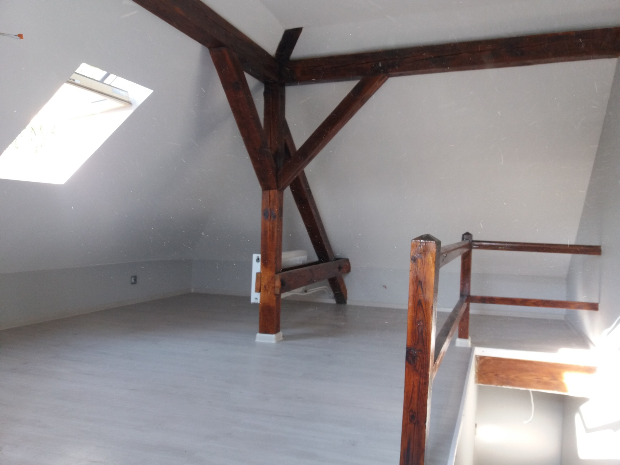 Poddasze z drewnianą konstrukcją nośną i oknem dachowym, wykończone panelami podłogowymi i pomalowane na szaro.