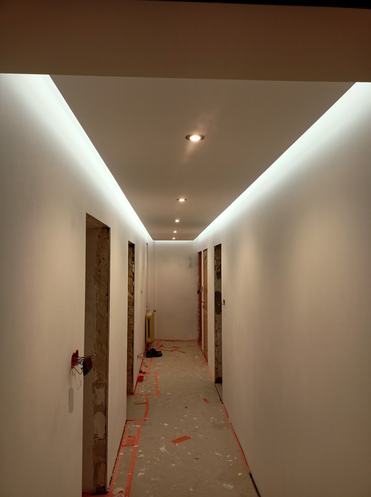Korytarz po remoncie z oświetleniem LED w suficie podwieszanym. Widoczne ślady prac na podłodze i niedokończone ościeżnice.