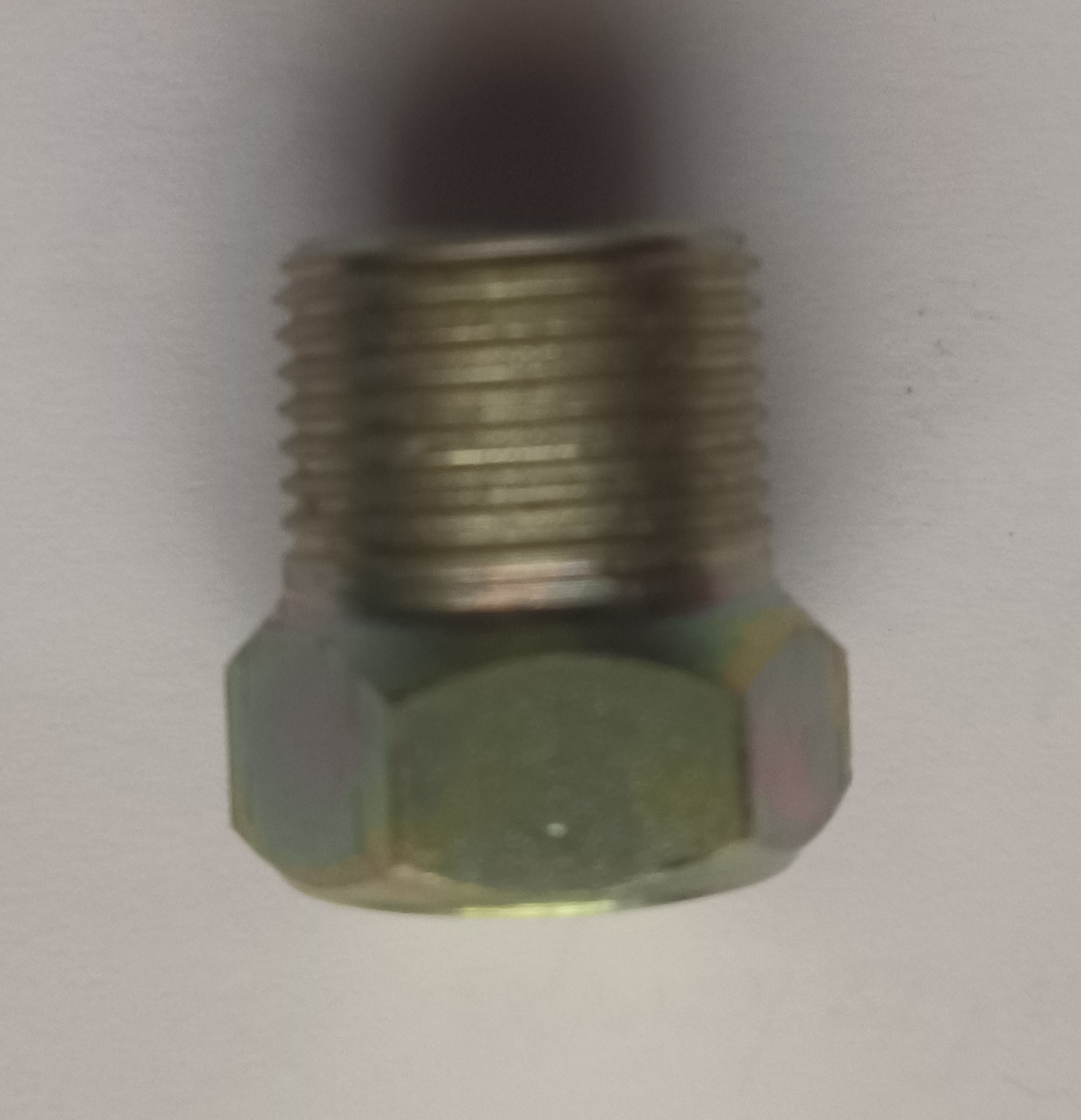 Metalowa śruba z gwintem i sześciokątną podstawą, pokryta żółtawą powłoką, leżąca na jasnym tle.