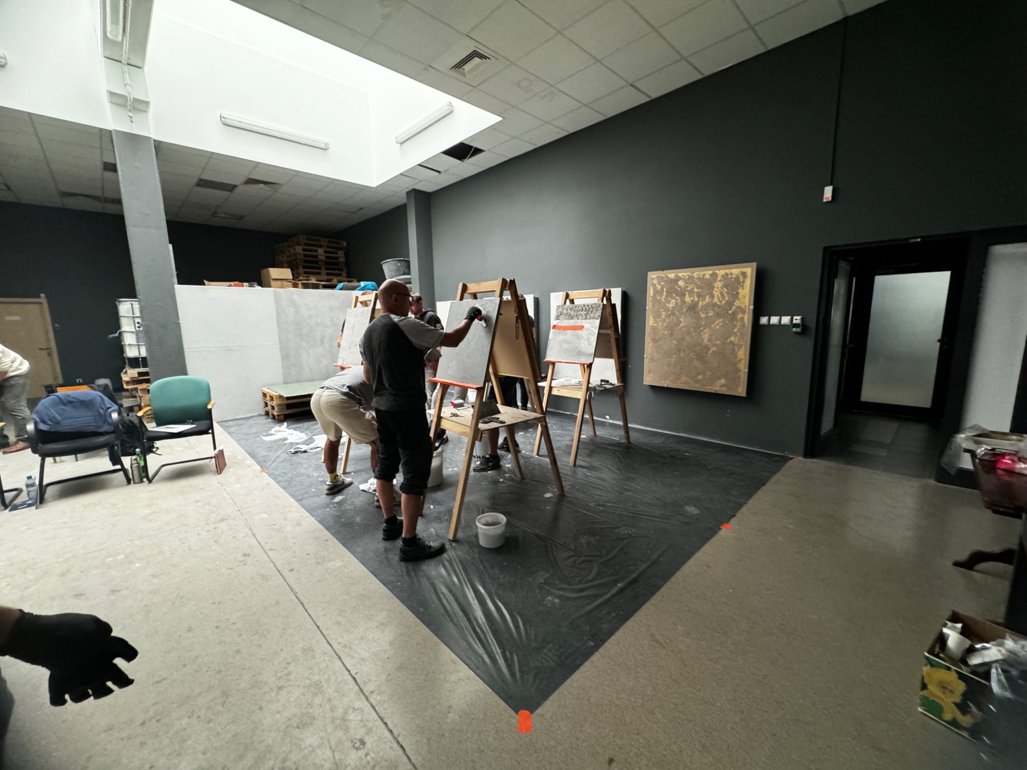 Szkolenie z aplikacji dekoracyjnych powłok na ścianę i podłogę, uczestnicy pracują na sztalugach z próbkami w przestronnym, jasnym pomieszczeniu.