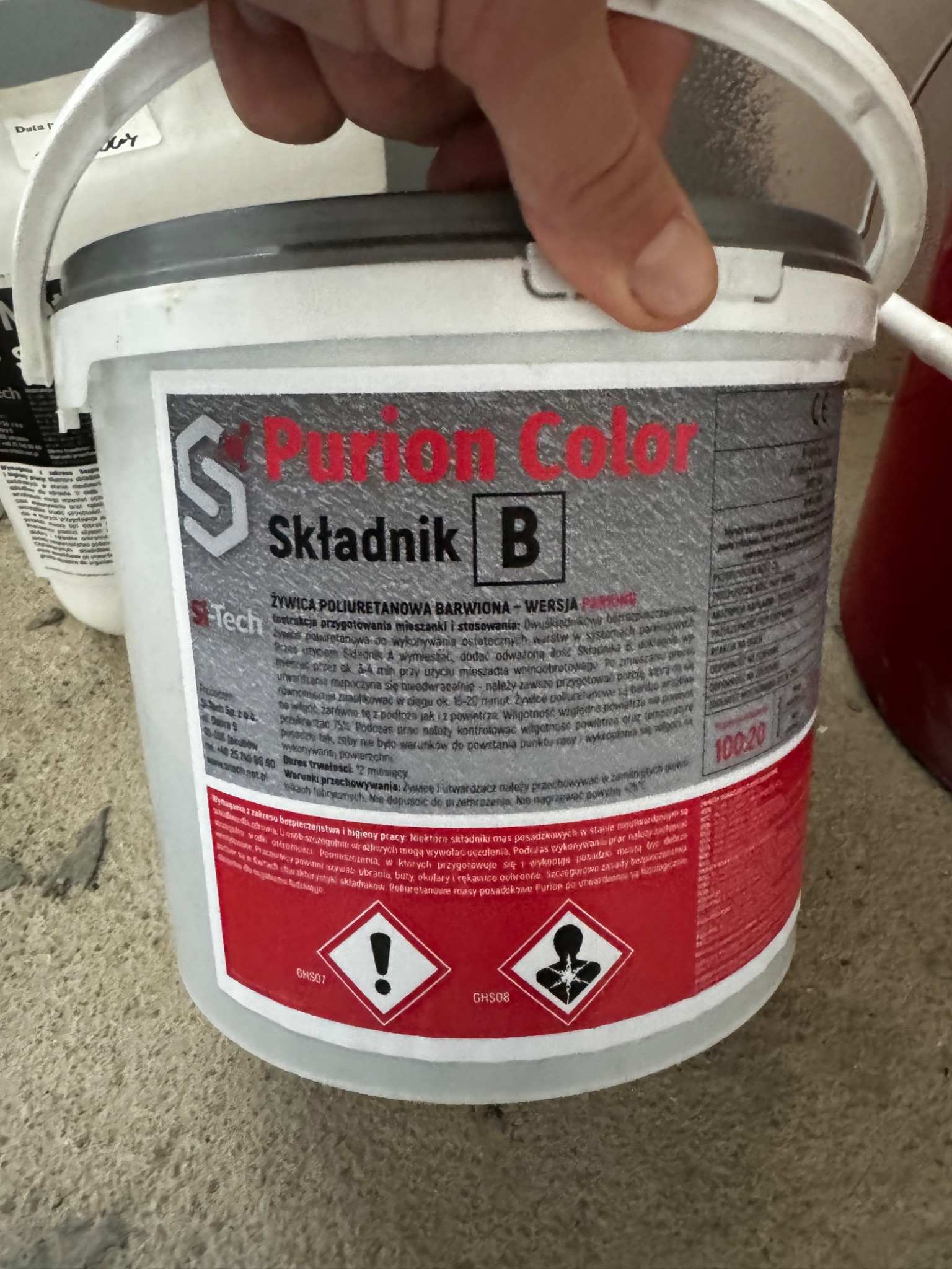 Białe wiadro z napisem Purion Color Składnik B, zawierające żywicę poliuretanową barwioną, widoczne ostrzeżenia BHP