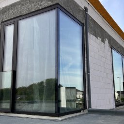 WINLUX Jakub Turowski - Nowoczesne okno narożne z czarną ramą w surowym stanie budynku, z widocznym ociepleniem i elementami konstrukcyjnymi.