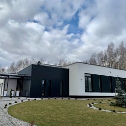 WINLUX Jakub Turowski - Nowoczesny dom jednorodzinny z czarną i białą elewacją, widoczne okna z czarnymi ramami i minimalistyczny ogród z trawnikiem i ozdobnymi kamieniami.