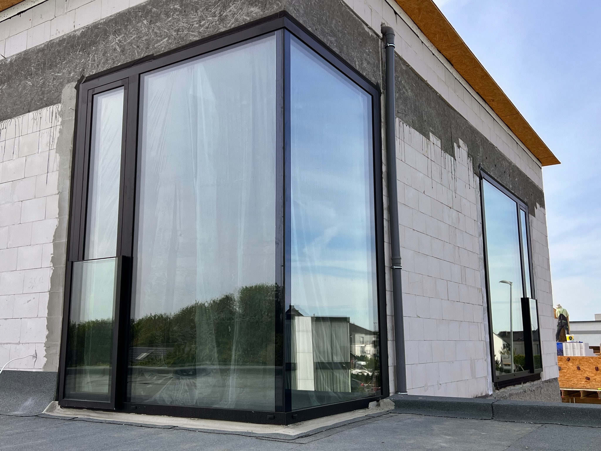 Nowoczesne okno narożne z czarną ramą w surowym stanie budynku, z widocznym ociepleniem i elementami konstrukcyjnymi.