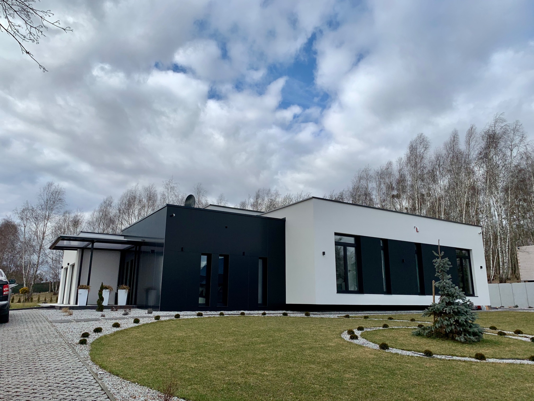 Nowoczesny dom jednorodzinny z czarną i białą elewacją, widoczne okna z czarnymi ramami i minimalistyczny ogród z trawnikiem i ozdobnymi kamieniami.