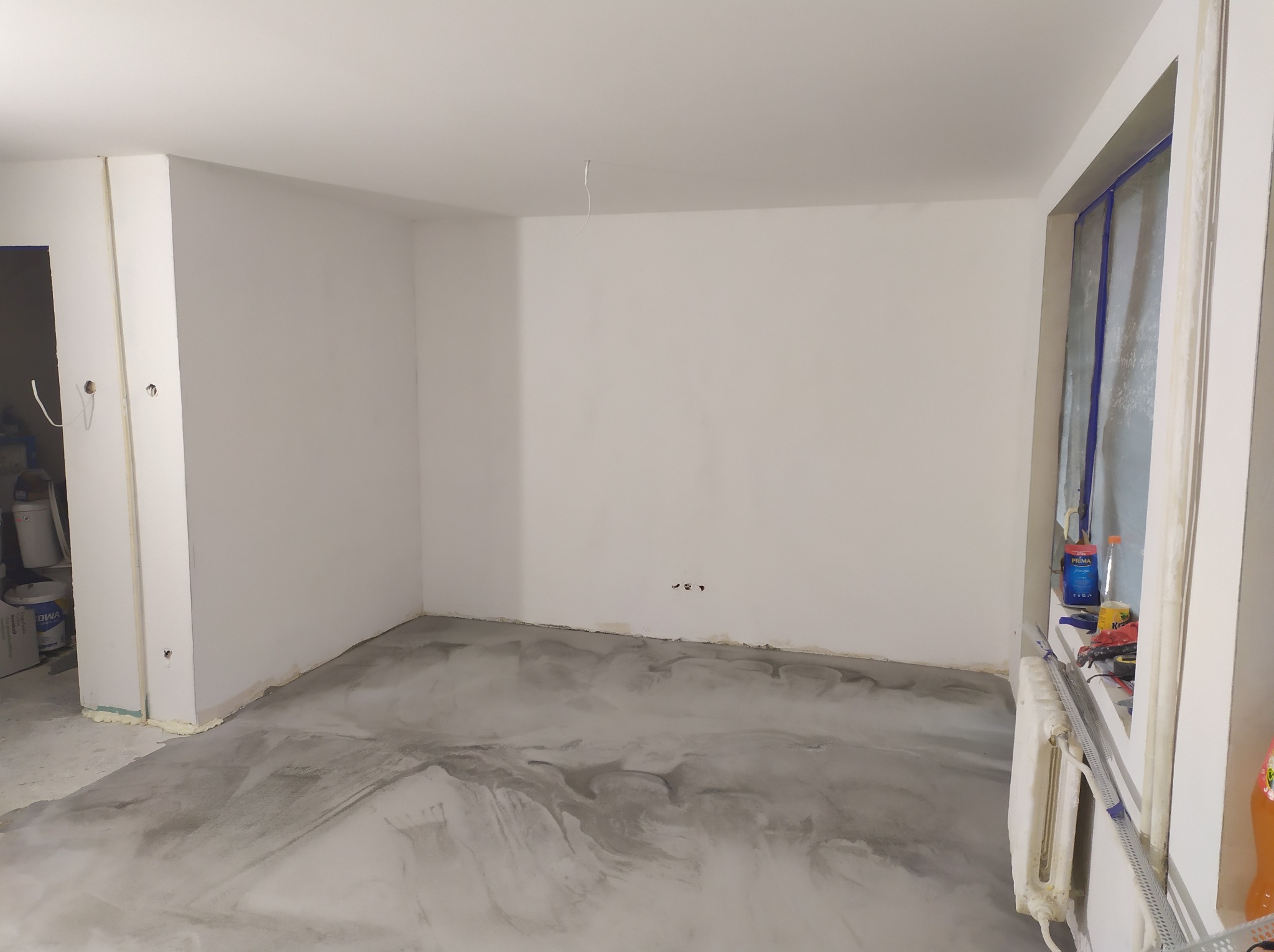 Pokój po wylaniu szarej, wzorzystej posadzki żywicznej, ściany pomalowane na biało, widoczne narzędzia i puszki z farbą przy oknie, zabezpieczone folią.