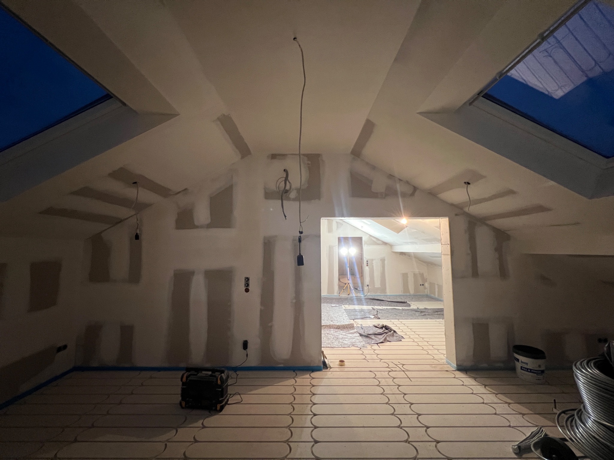 Poddasze w trakcie prac wykończeniowych: widoczne płyty karton-gips na ścianach, instalacja ogrzewania podłogowego i okna dachowe. Przygotowanie do dalszych prac.