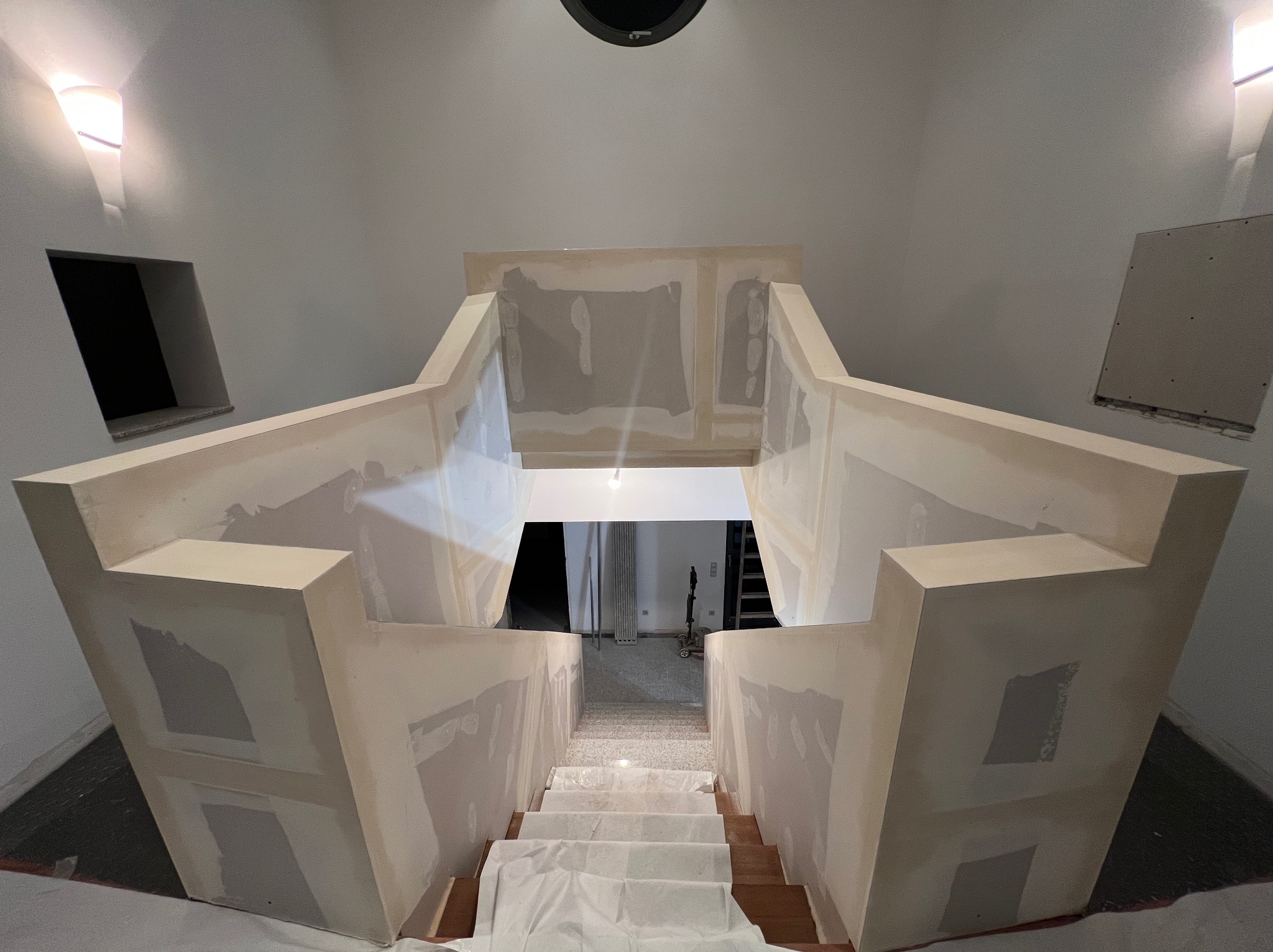 Klatka schodowa w trakcie wykończenia: ściany z płyt karton-gips, widoczne łączenia wymagające szpachlowania. Schody zabezpieczone folią malarską.