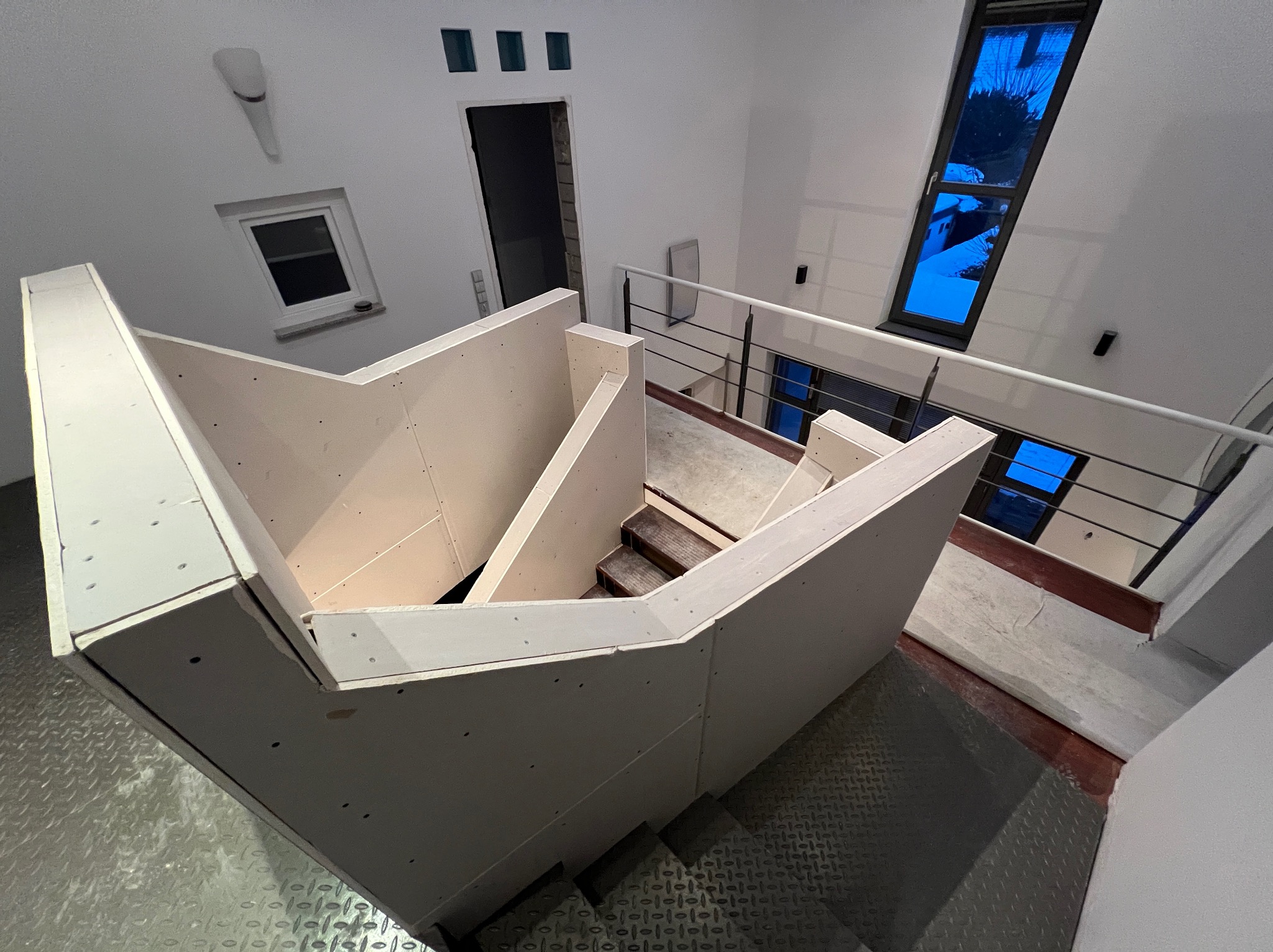 Montaż płyt karton-gips na schodach w nowoczesnym wnętrzu. Widok z góry ukazuje konstrukcję przed wykończeniem, z widocznymi elementami mocującymi i metalową podłogą.