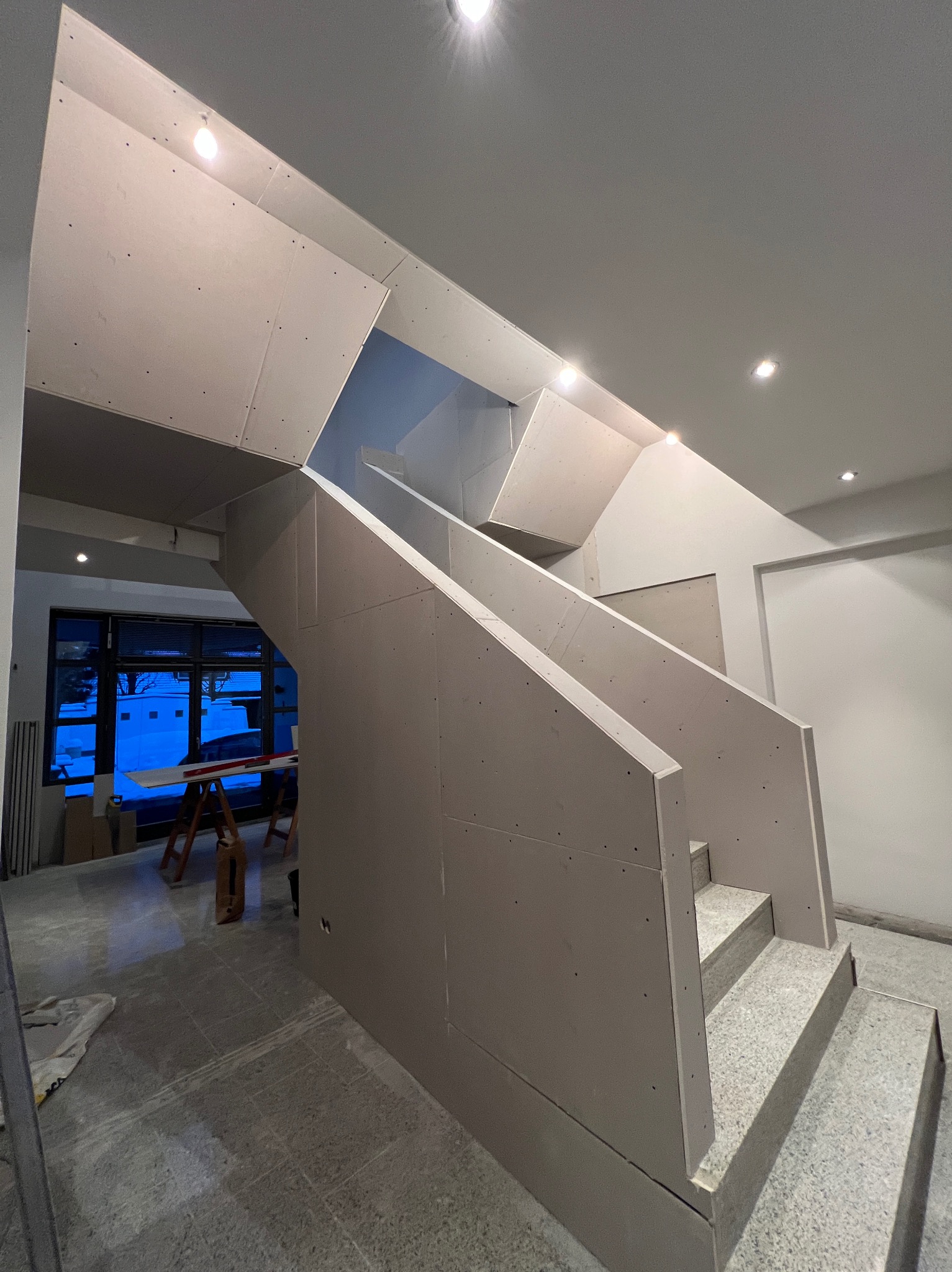 Montaż płyt G-K na schodach i suficie w Gdańsku. Widoczne profile i płyty, surowe wykończenie. Prace wykończeniowe w trakcie realizacji, oświetlenie punktowe.