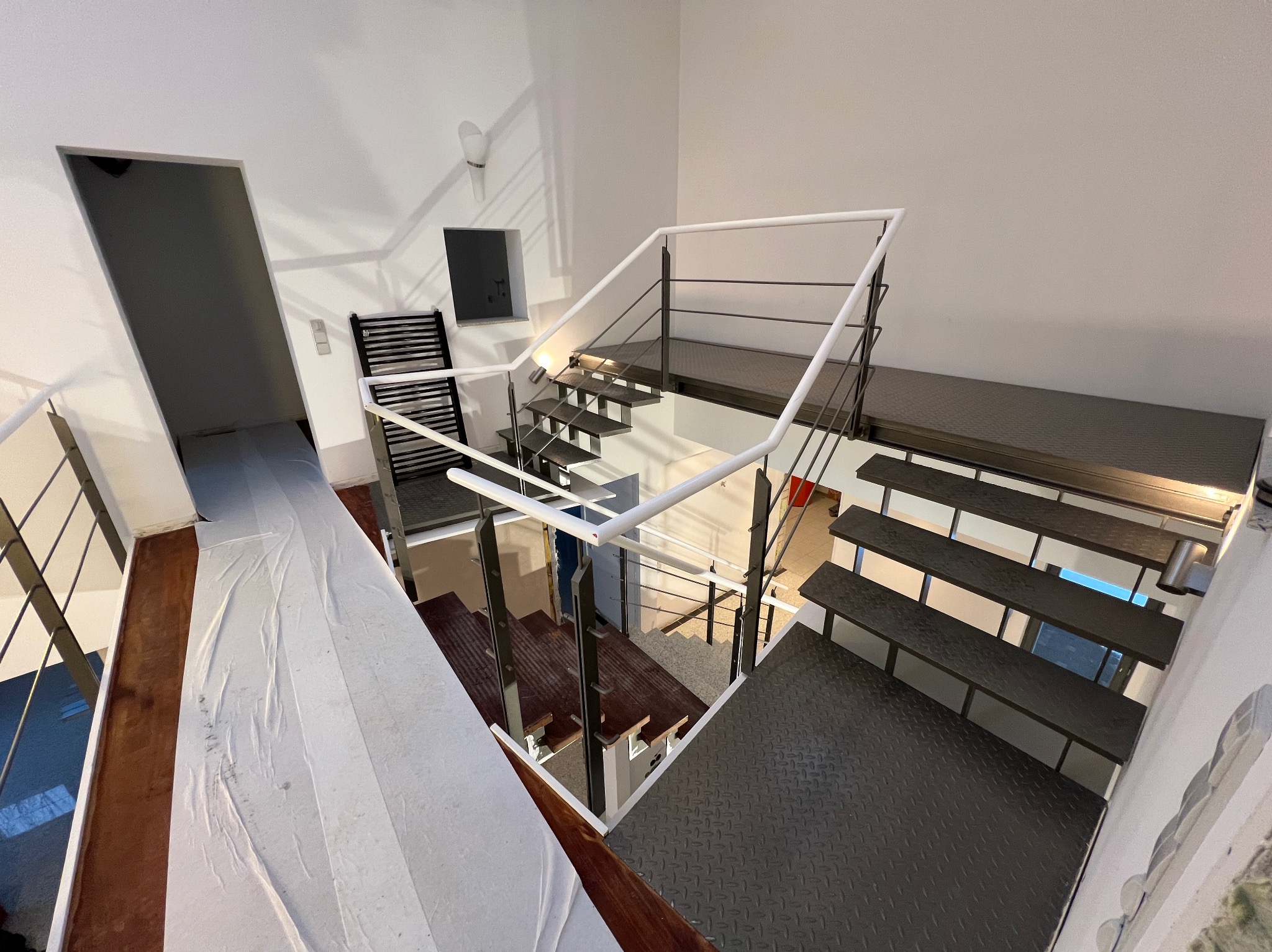 Nowoczesne schody z metalowymi stopniami i białymi balustradami, widok z góry. Świeżo wyremontowane wnętrze z białymi ścianami i widocznym grzejnikiem.