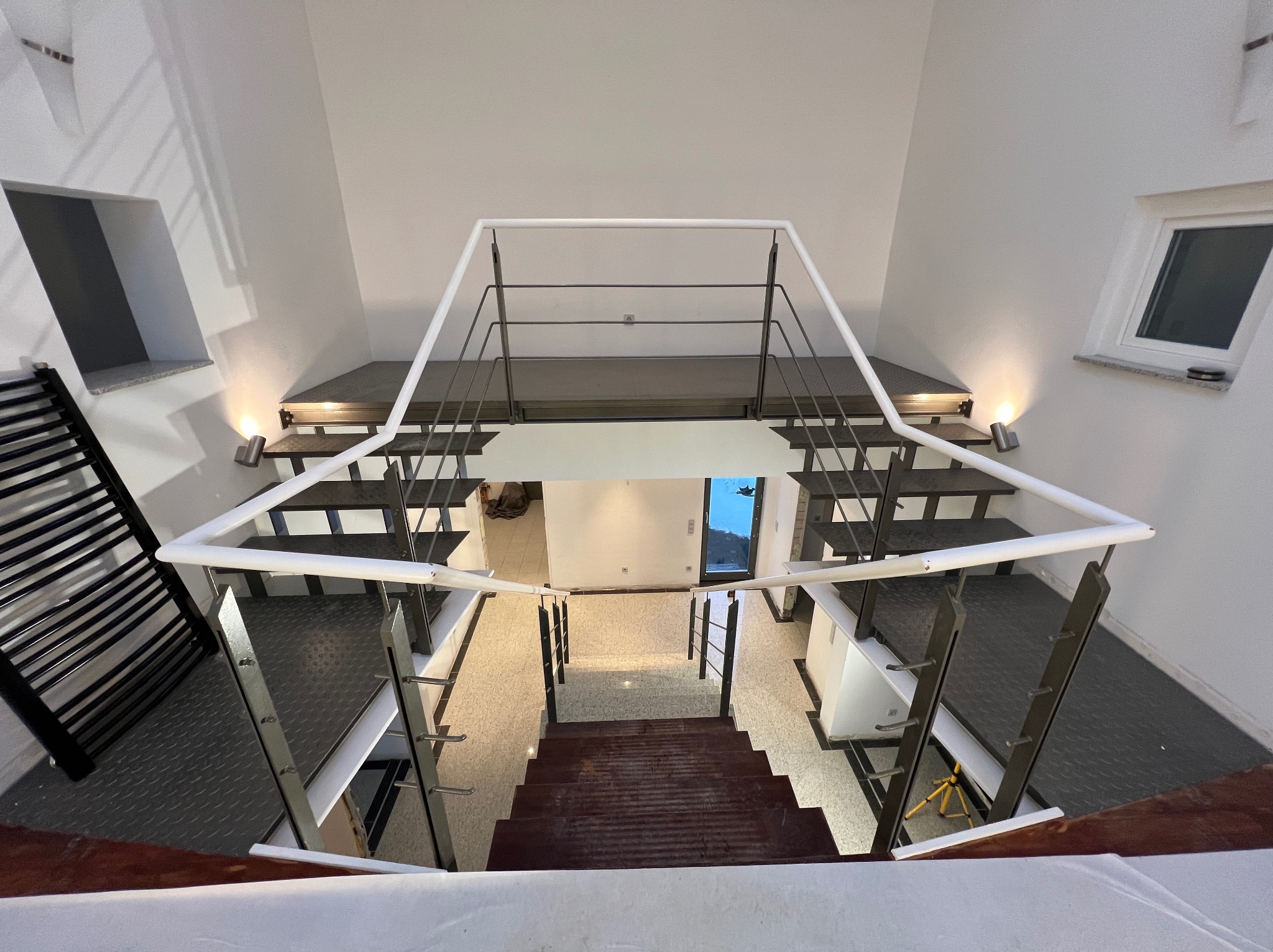 Nowoczesne schody z metalowymi stopniami i białymi ścianami, widok z góry. Minimalistyczny design z oświetleniem punktowym i kontrastującymi materiałami.