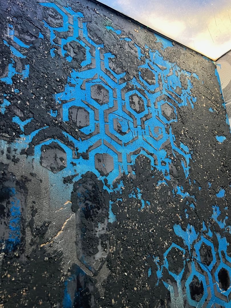 Nierówna ściana z dekoracyjnym wzorem sześciokątów w kolorze niebieskim i czarnym, widoczne ślady farby i niedoskonałości, surowy styl wykończenia.