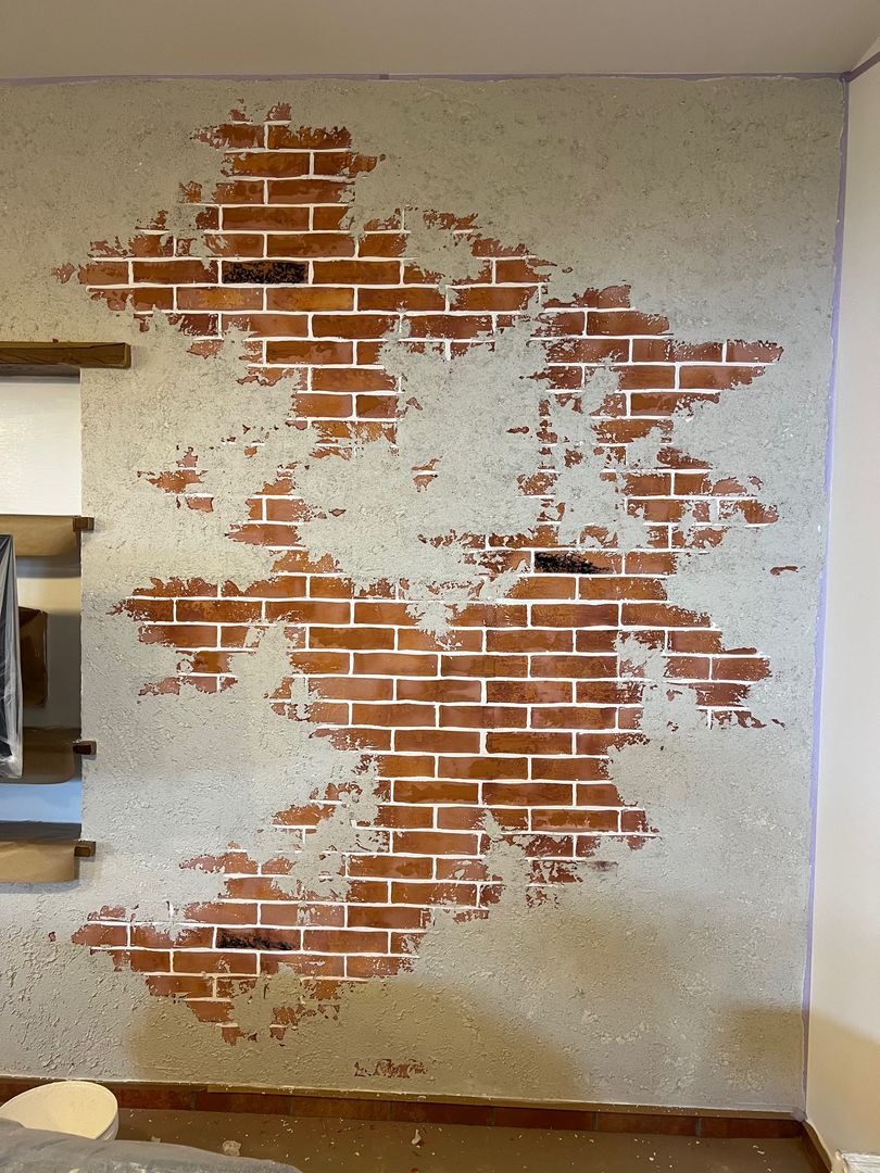 Dekoracyjna ściana z efektem odsłoniętej cegły, imitująca starą strukturę, z fragmentami szarego tynku i widocznymi czerwonymi cegłami z białą fugą.