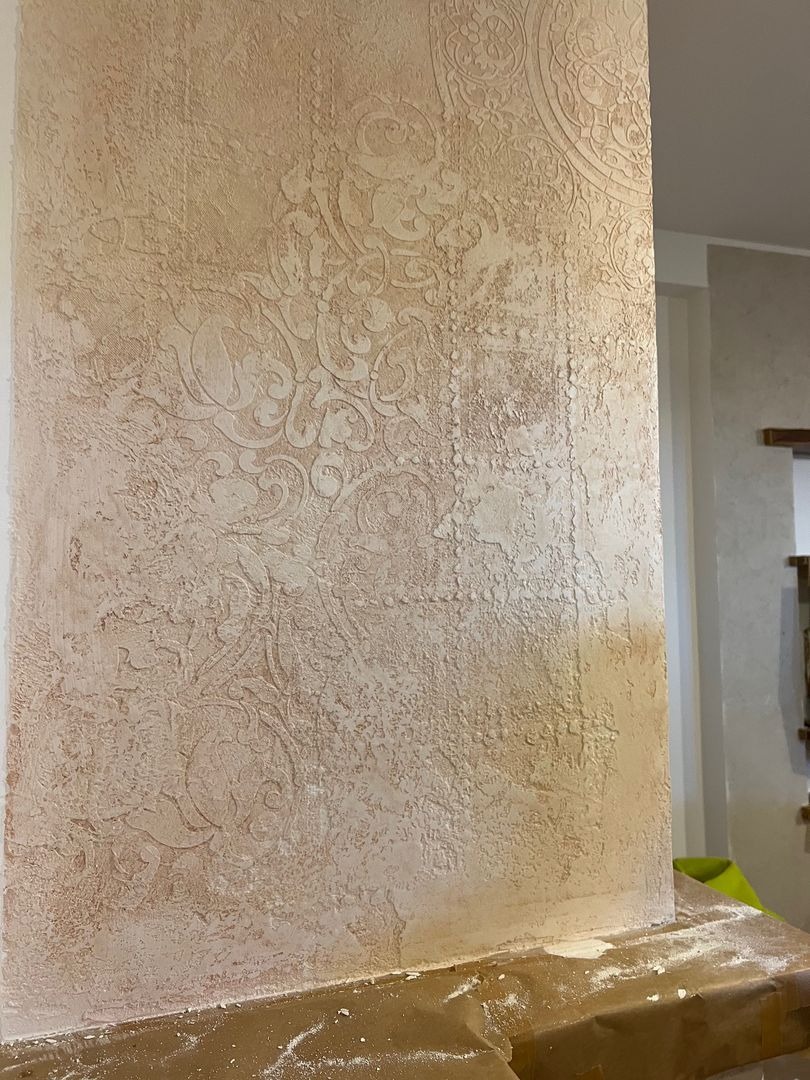 Beżowa ściana z dekoracyjną, wypukłą fakturą w stylu vintage, zabezpieczona folią malarską u dołu.