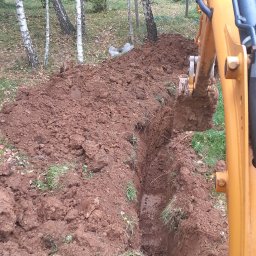 Usługi ogólnobudowlane mini koparką - Wykopany rów w Ustrzykach Dolnych, widoczny fragment koparki i drzewa w tle, ziemia brązowa, na dnie rowu woda.