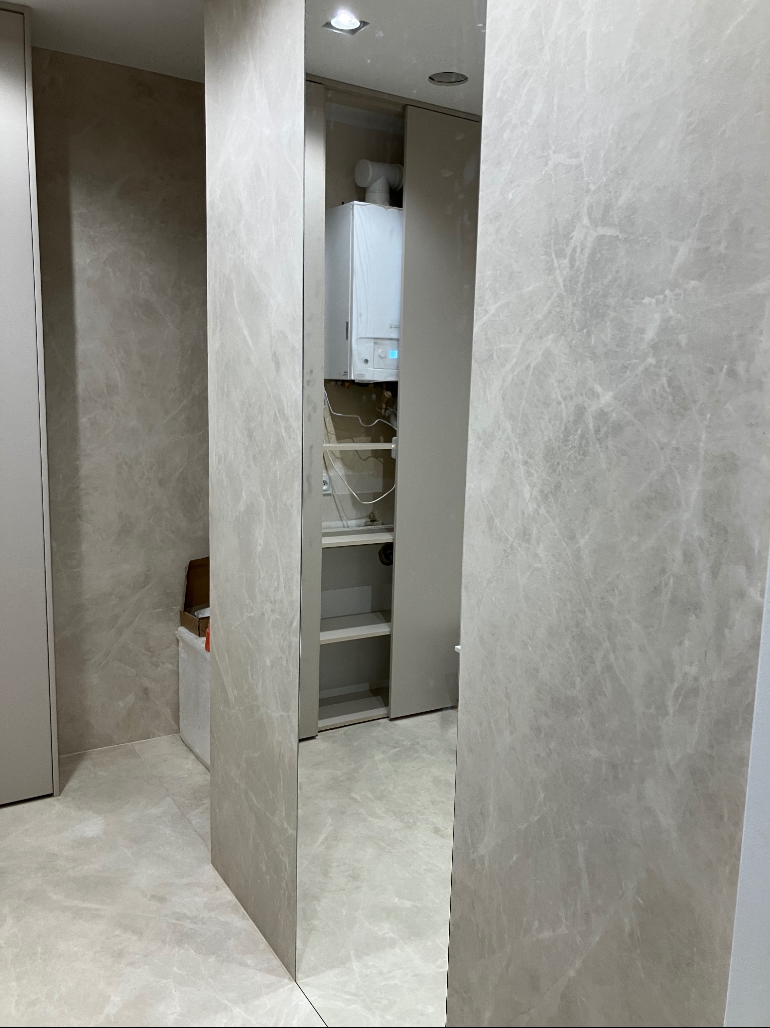 Wnętrze garderoby w trakcie montażu z widocznym piecem gazowym, półkami i marmurkową okładziną ścian oraz lustrzanym panelem.