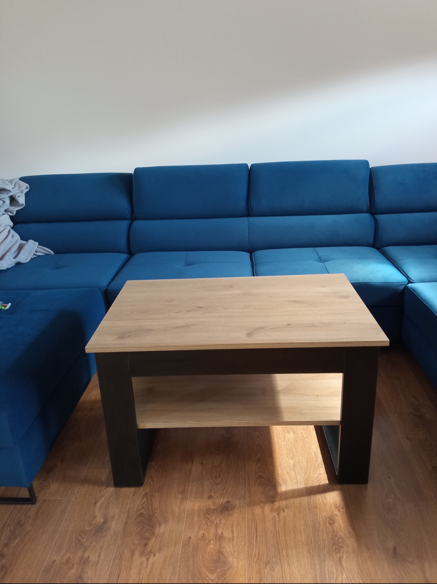 Niebieski narożnik z drewnianym stolikiem kawowym z półką, ustawione na panelach podłogowych.