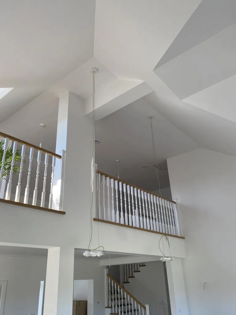 Wnętrze domu po remoncie, świeżo pomalowane na biało, z dwukondygnacyjnym holem, białymi balustradami z drewnianymi poręczami i nowoczesnymi lampami wiszącymi.