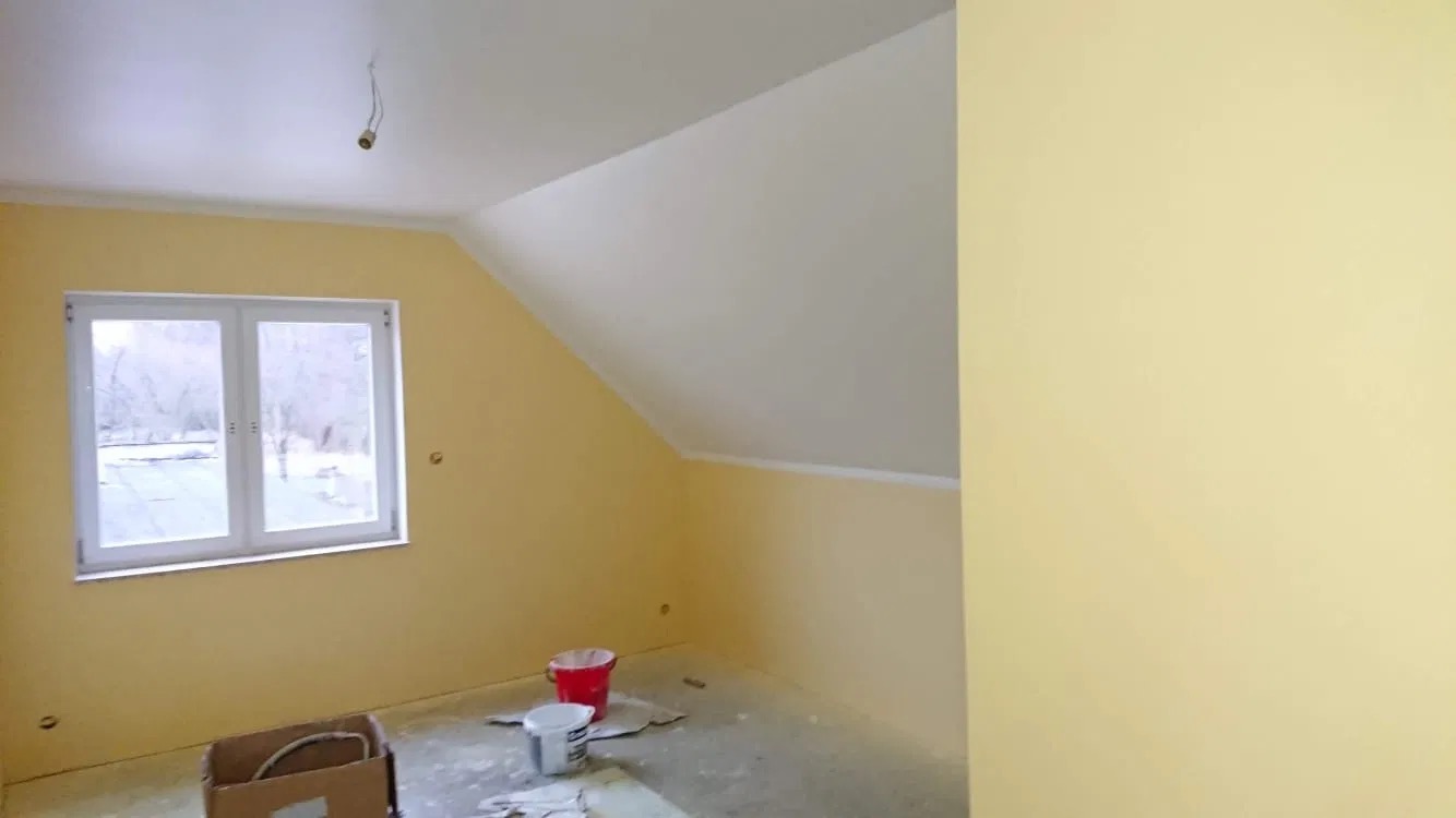 Pokój na poddaszu w Gowarczowie po częściowym odświeżeniu: ściany pomalowane na żółto, sufit na biało, widoczne ślady po pracach malarskich na podłodze i narzędzia w kartonie.